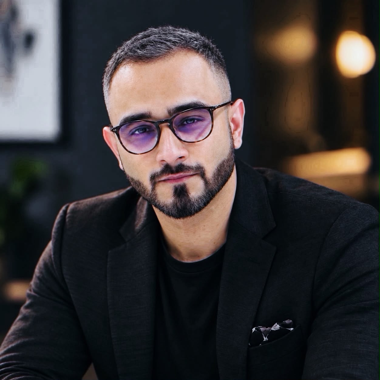Portrait of a man wearing glasses and a black jacket.